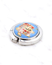 Silver metal table-top bag hanger featuring a red daruma doll on a blue background with metallic gold accents.