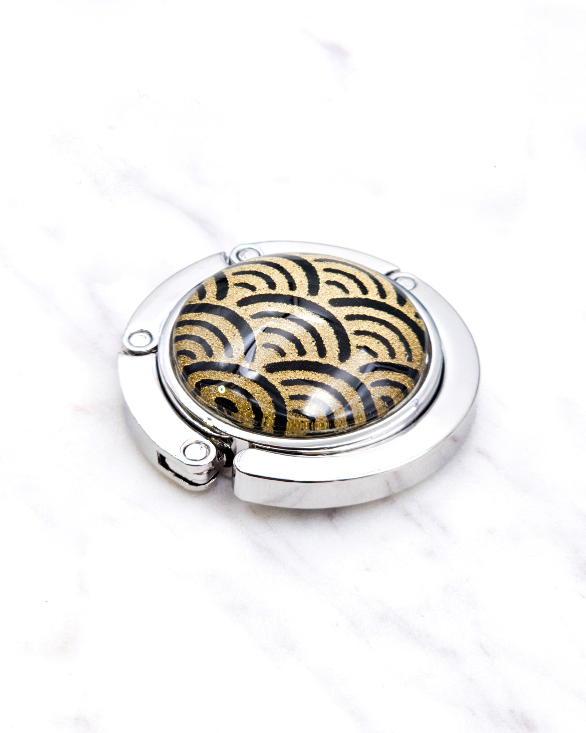 Silver metal table-top bag hanger featuring a traditional gold and black seigaiha (wave crests) design.