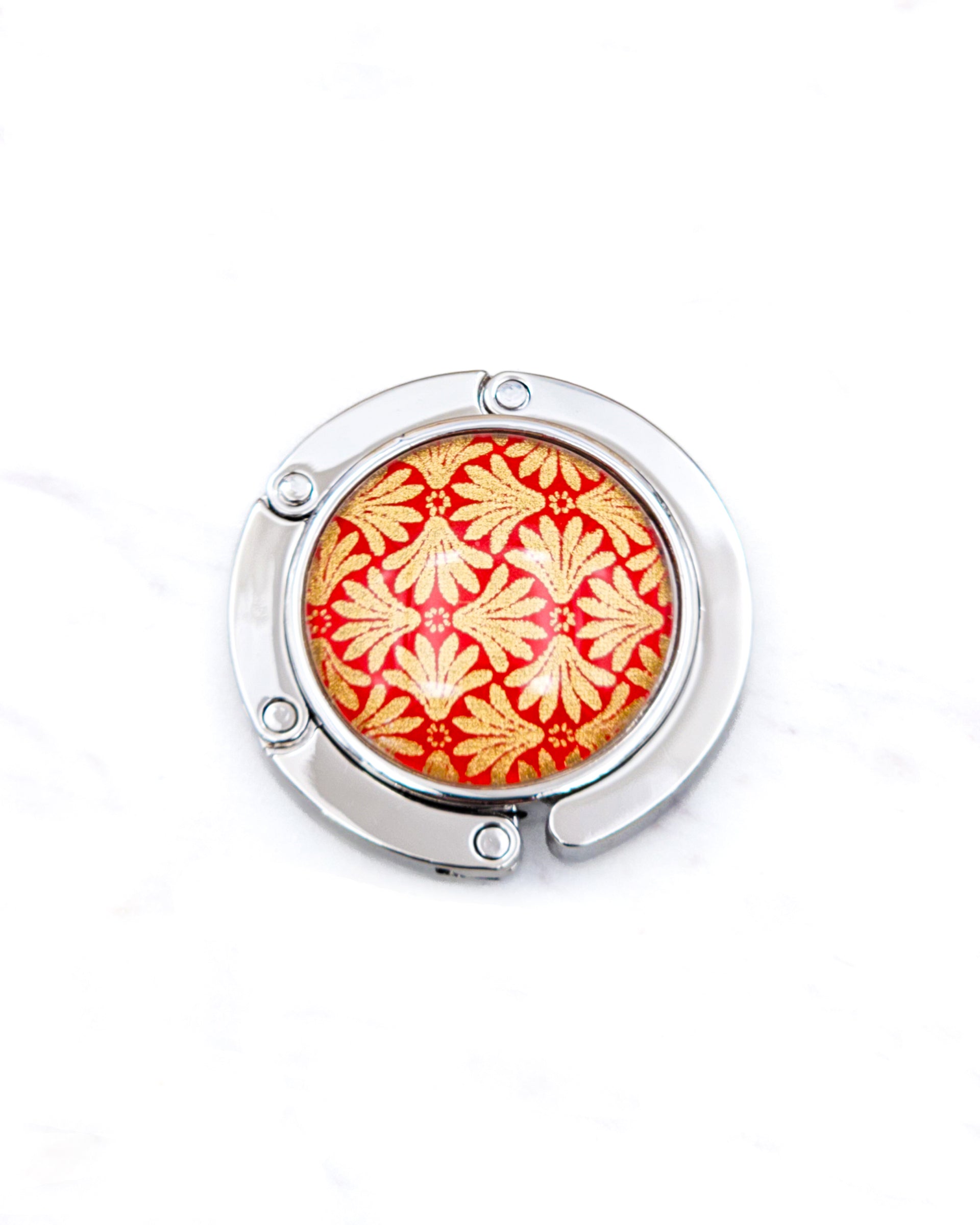 Round silver metal table-top bag hanger featuring a metallic gold motif on a red background.