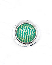 Round silver metal tabletop bag hanger featuring a metallic gold traditional Japanese sayagata design on a green background.