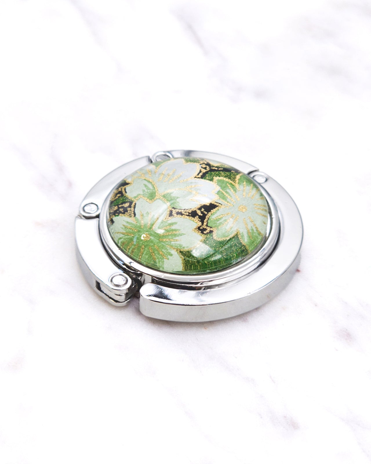 Silver metal table-top bag hanger featuring green cherry blossoms on a green background with metallic gold accents.