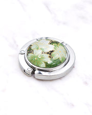 Silver metal table-top bag hanger featuring green cherry blossoms on a green background with metallic gold accents.