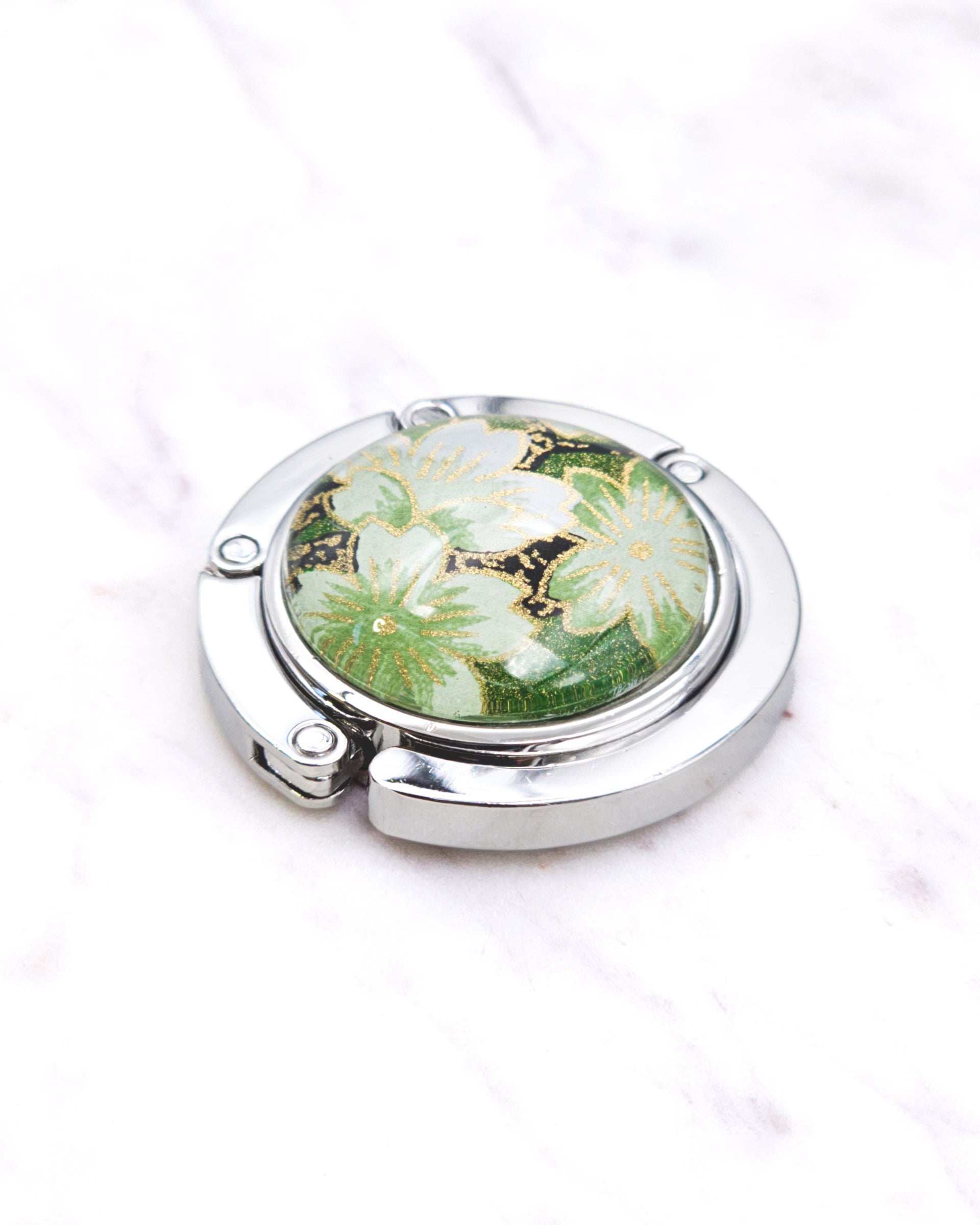 Silver metal table-top bag hanger featuring green cherry blossoms on a green background with metallic gold accents.