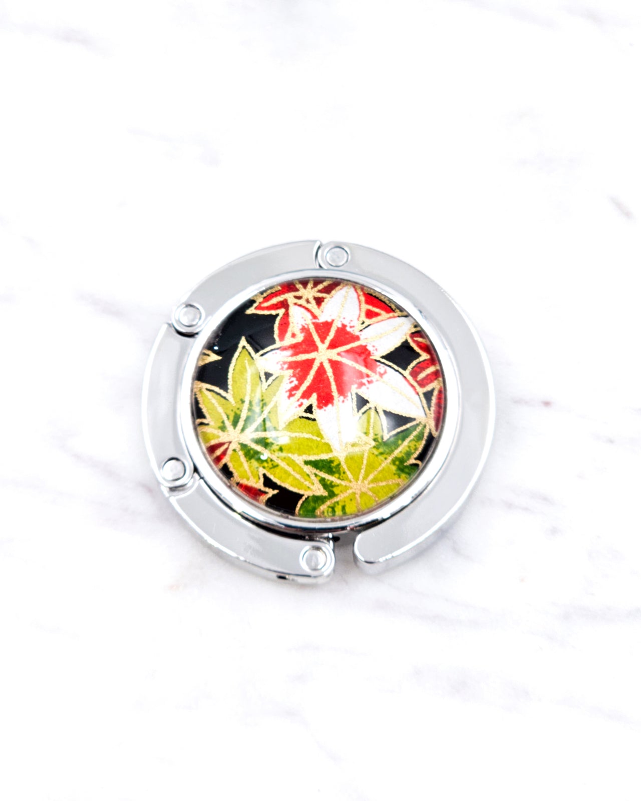 Silver metal table-top bag hanger featuring green, red, and white maples leaves on a black background with metallic gold accents.