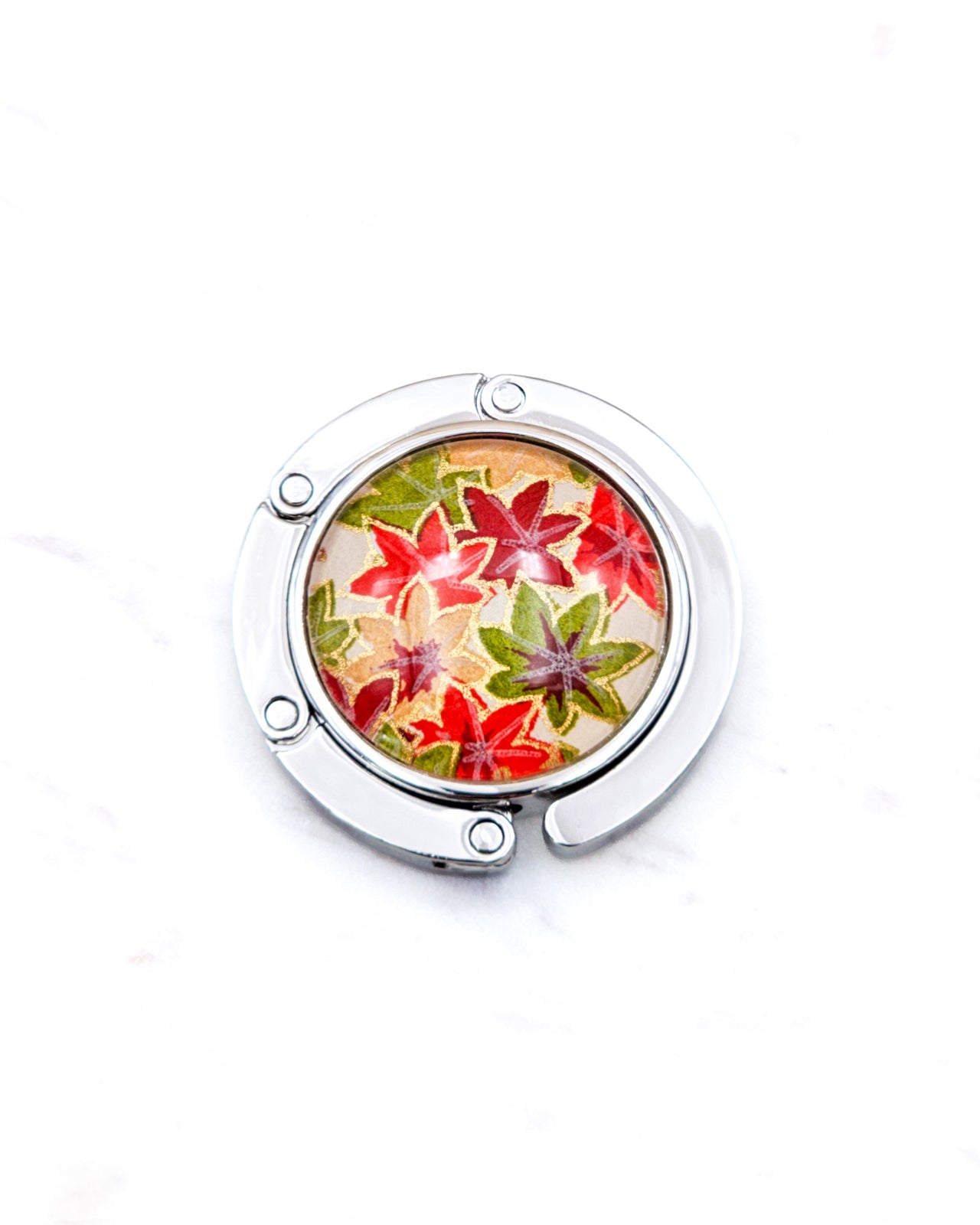 Round silver metal table-top bag hanger featuring small orange, green, and red Japanese maple leaves with metallic gold details.