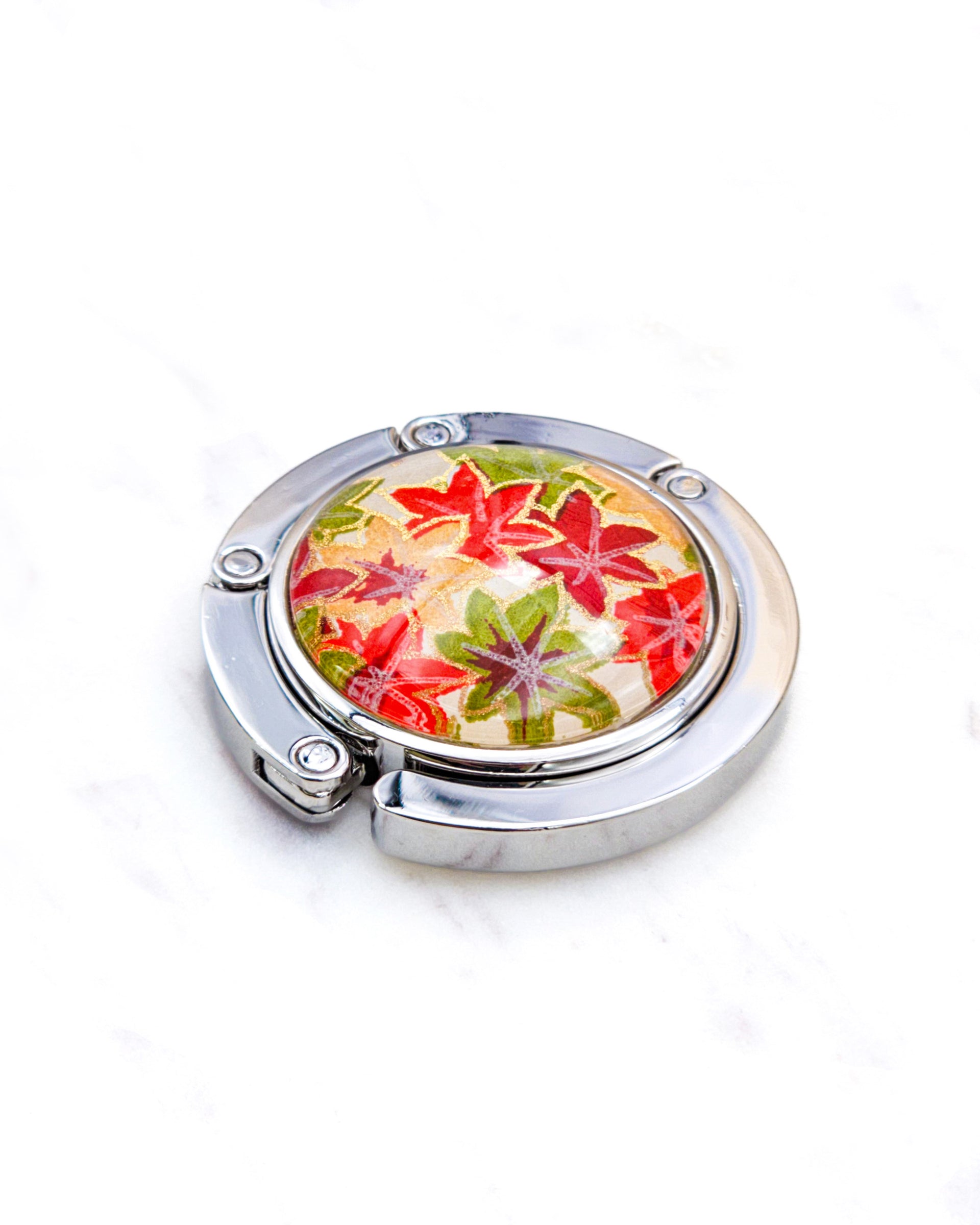 Round silver metal table-top bag hanger featuring small orange, green, and red Japanese maple leaves with metallic gold details.
