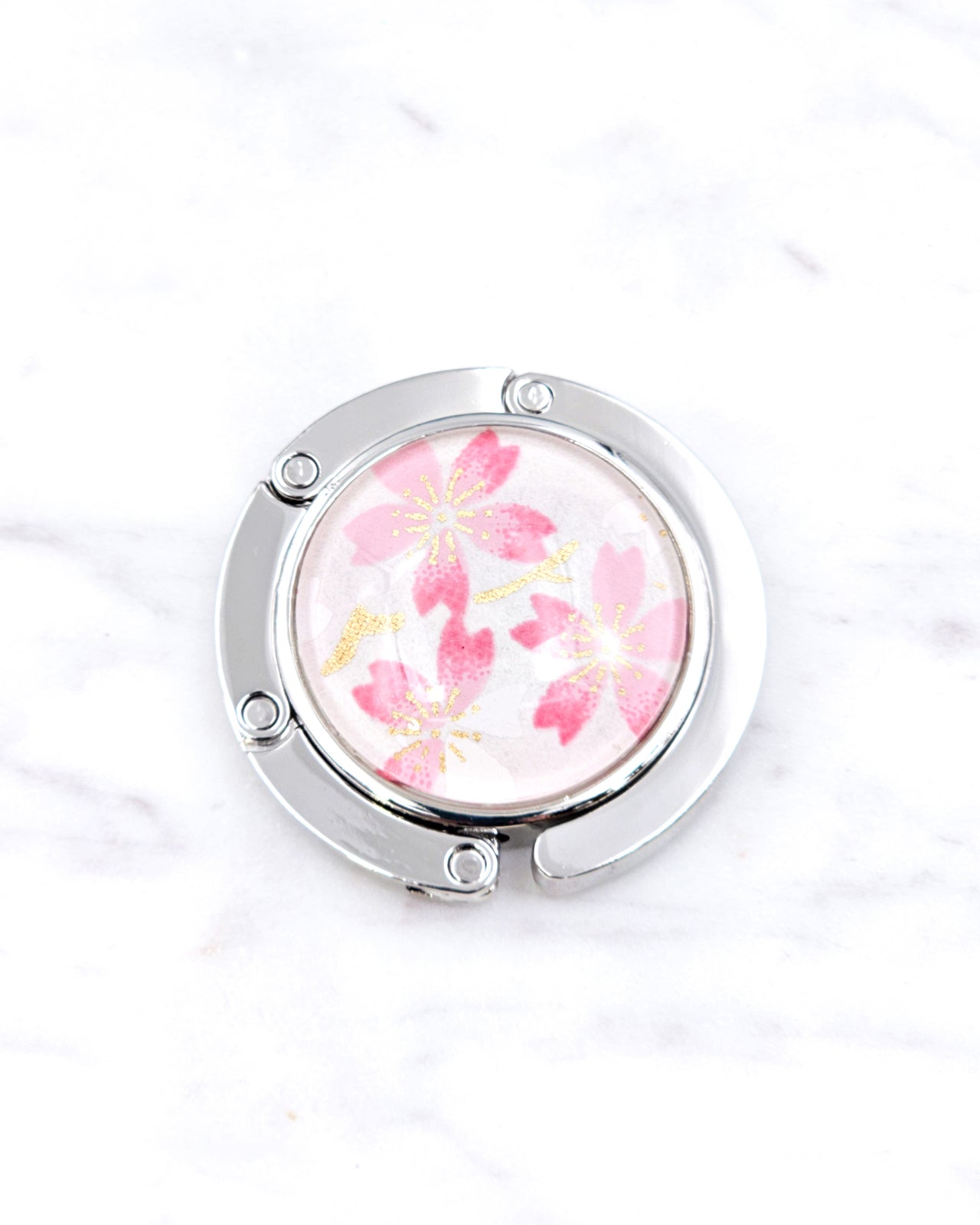 Silver metal table-top bag hanger featuring pink cherry blossoms on a white background with metallic gold accents.