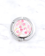 Silver metal table-top bag hanger featuring pink cherry blossoms on a white background with metallic gold accents.