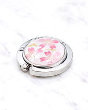 Silver metal table-top bag hanger featuring pink cherry blossoms on a white background with metallic gold accents.