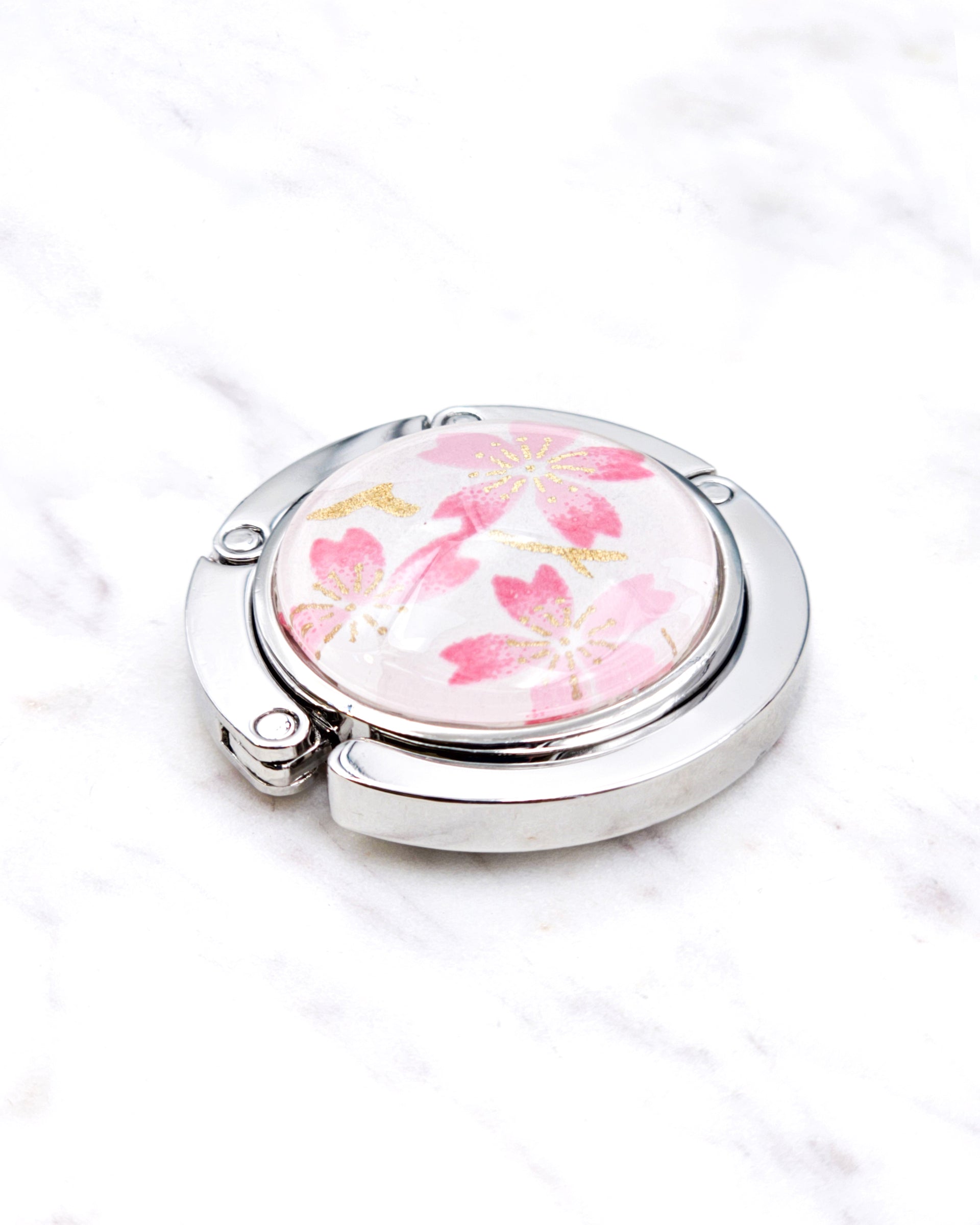 Silver metal table-top bag hanger featuring pink cherry blossoms on a white background with metallic gold accents.