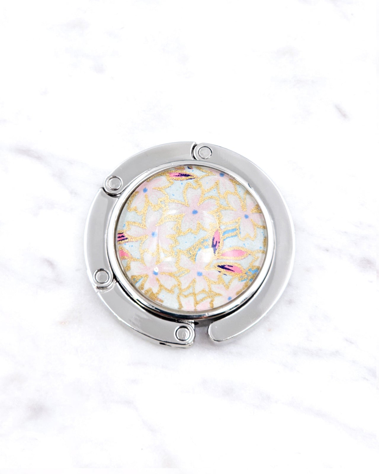 Silver metal table-top bag hanger featuring pink cherry blossoms on a light blue background with metallic gold accents.