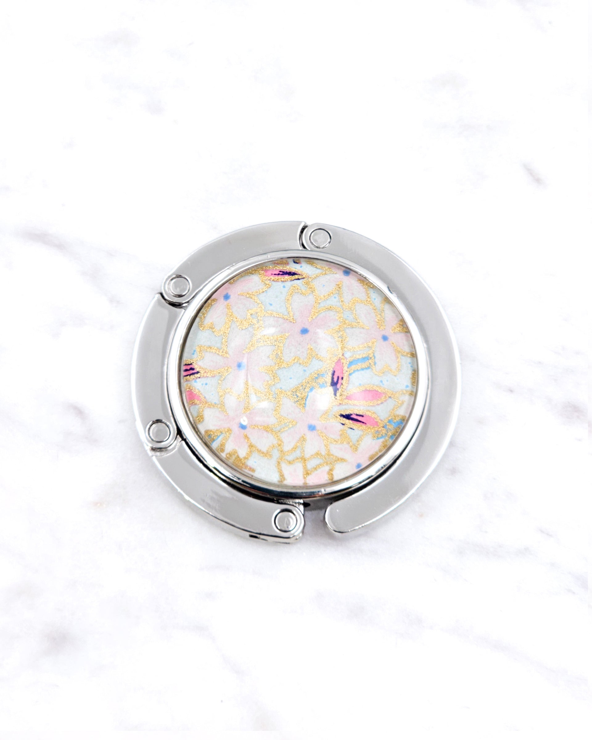 Silver metal table-top bag hanger featuring pink cherry blossoms on a light blue background with metallic gold accents.