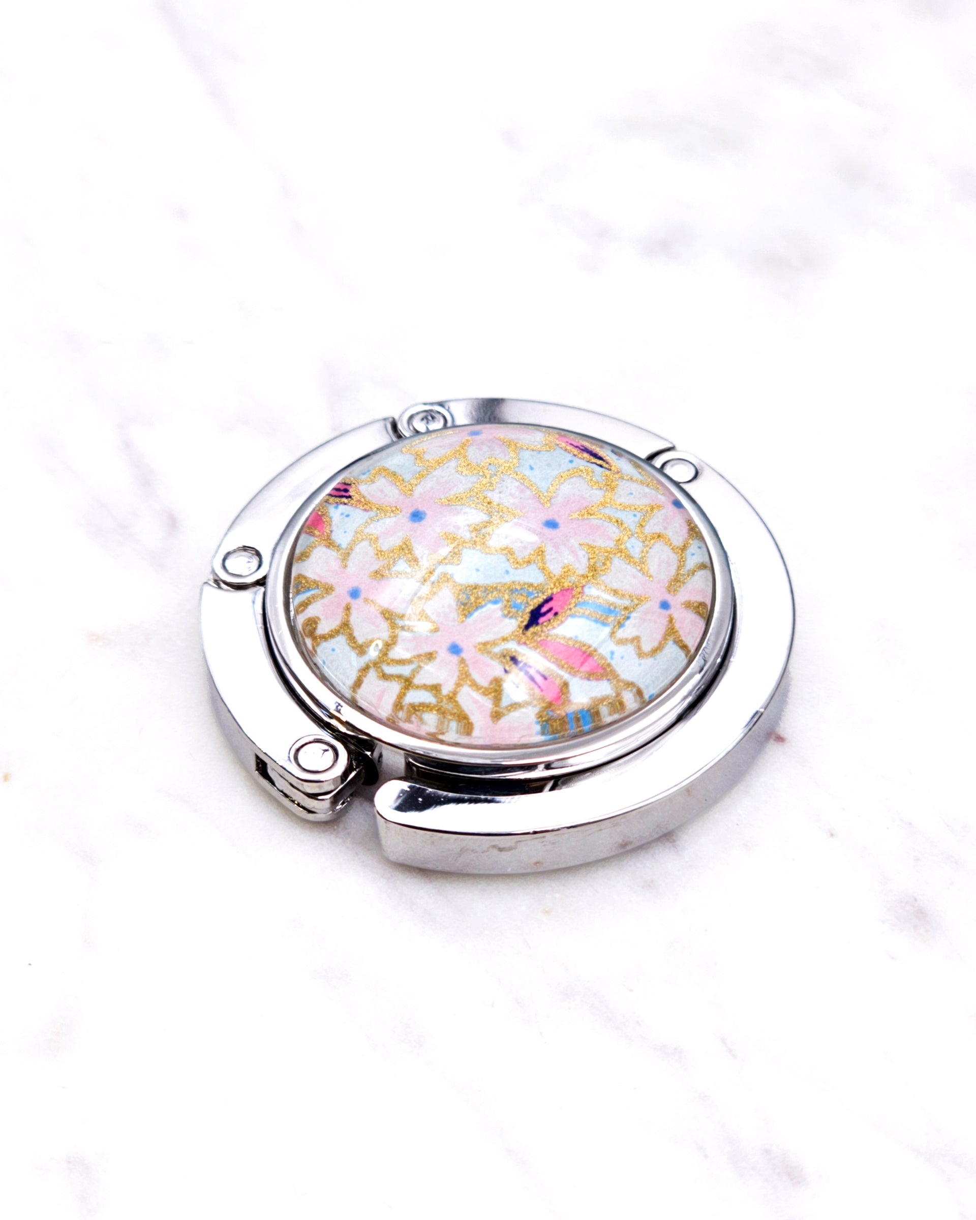 Silver metal table-top bag hanger featuring pink cherry blossoms on a light blue background with metallic gold accents.