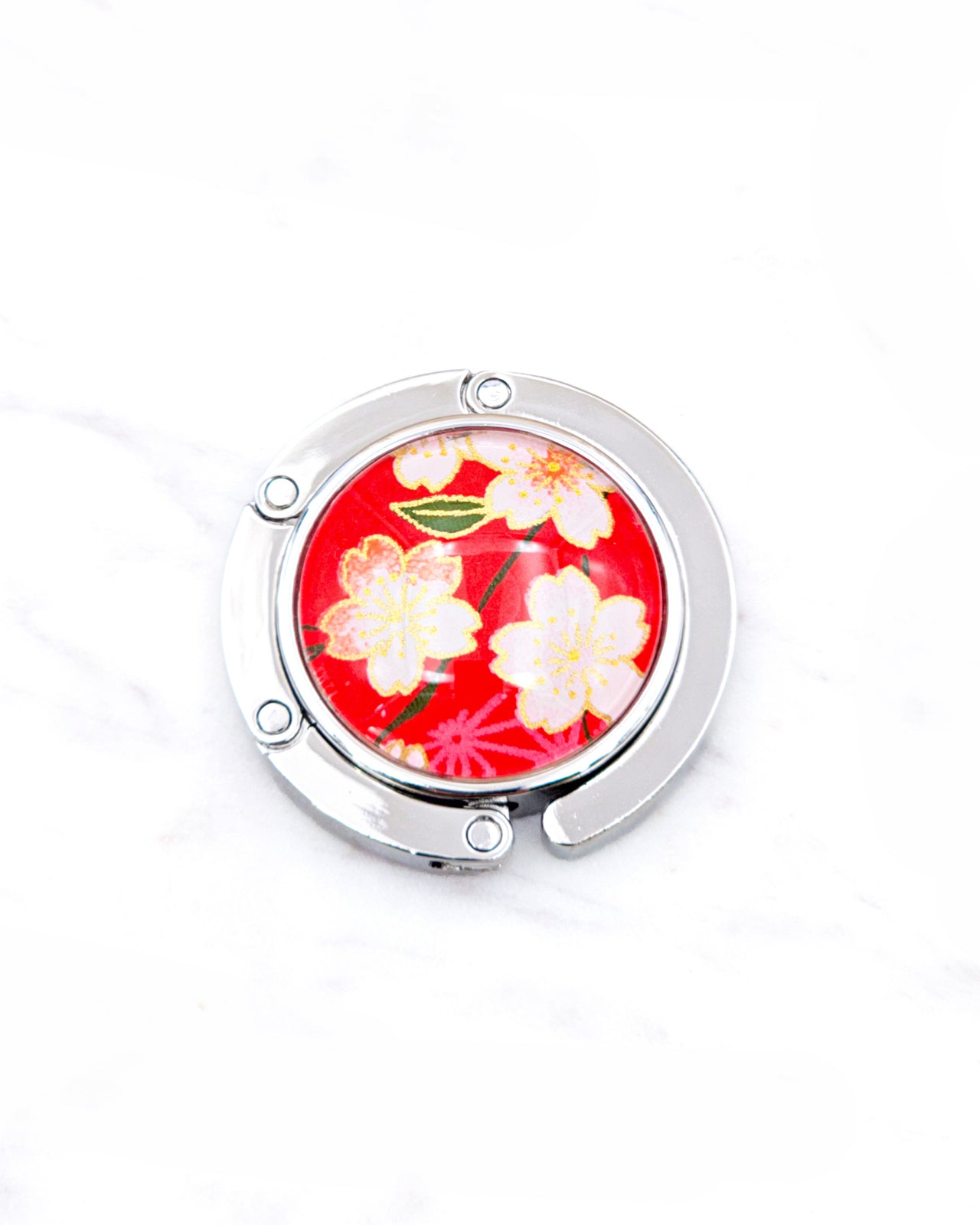 Round silver metal table-top bag hanger featuring pink and white cherry blossoms on a red background with metallic gold details.