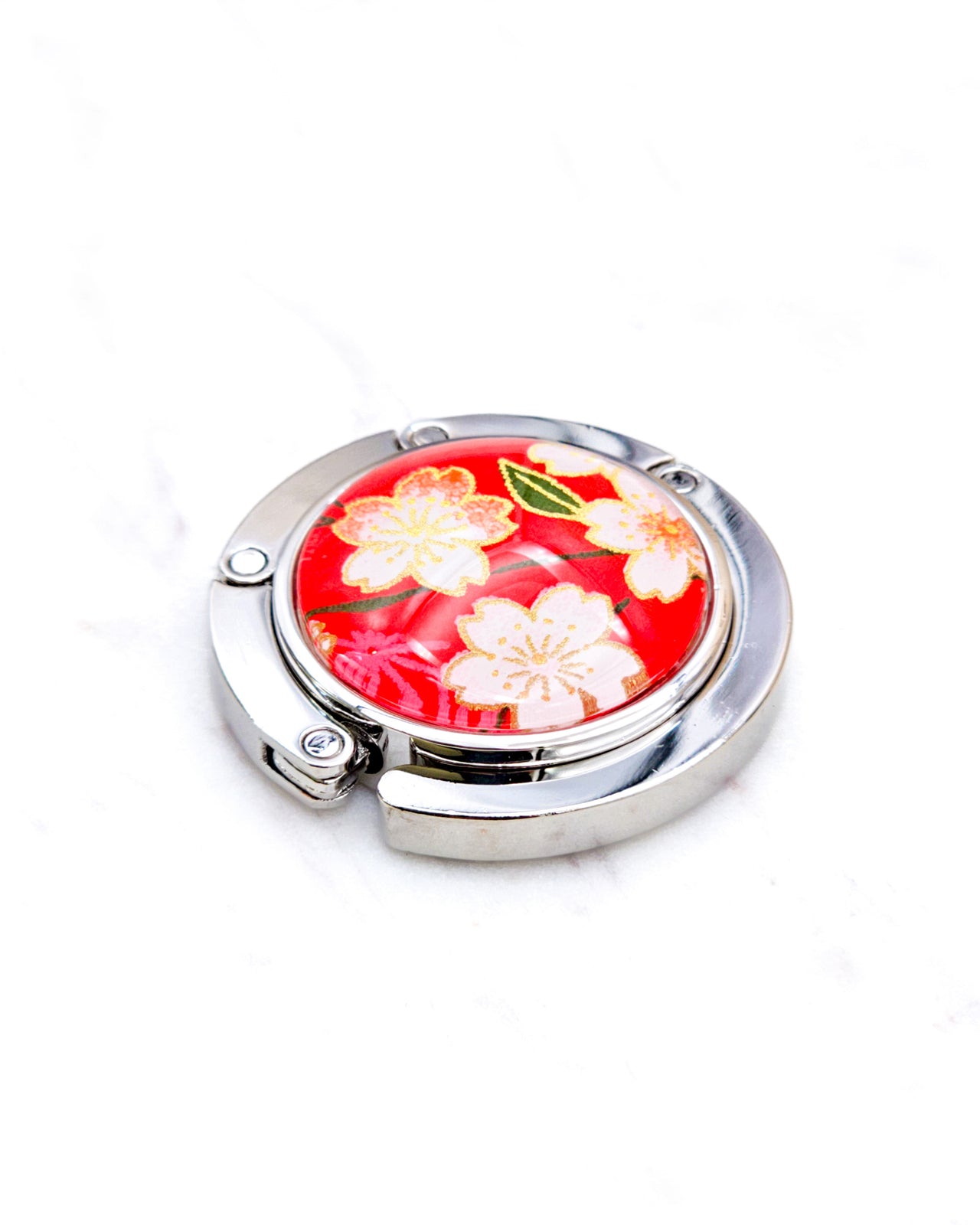 Round silver metal table-top bag hanger featuring pink and white cherry blossoms on a red background with metallic gold details.