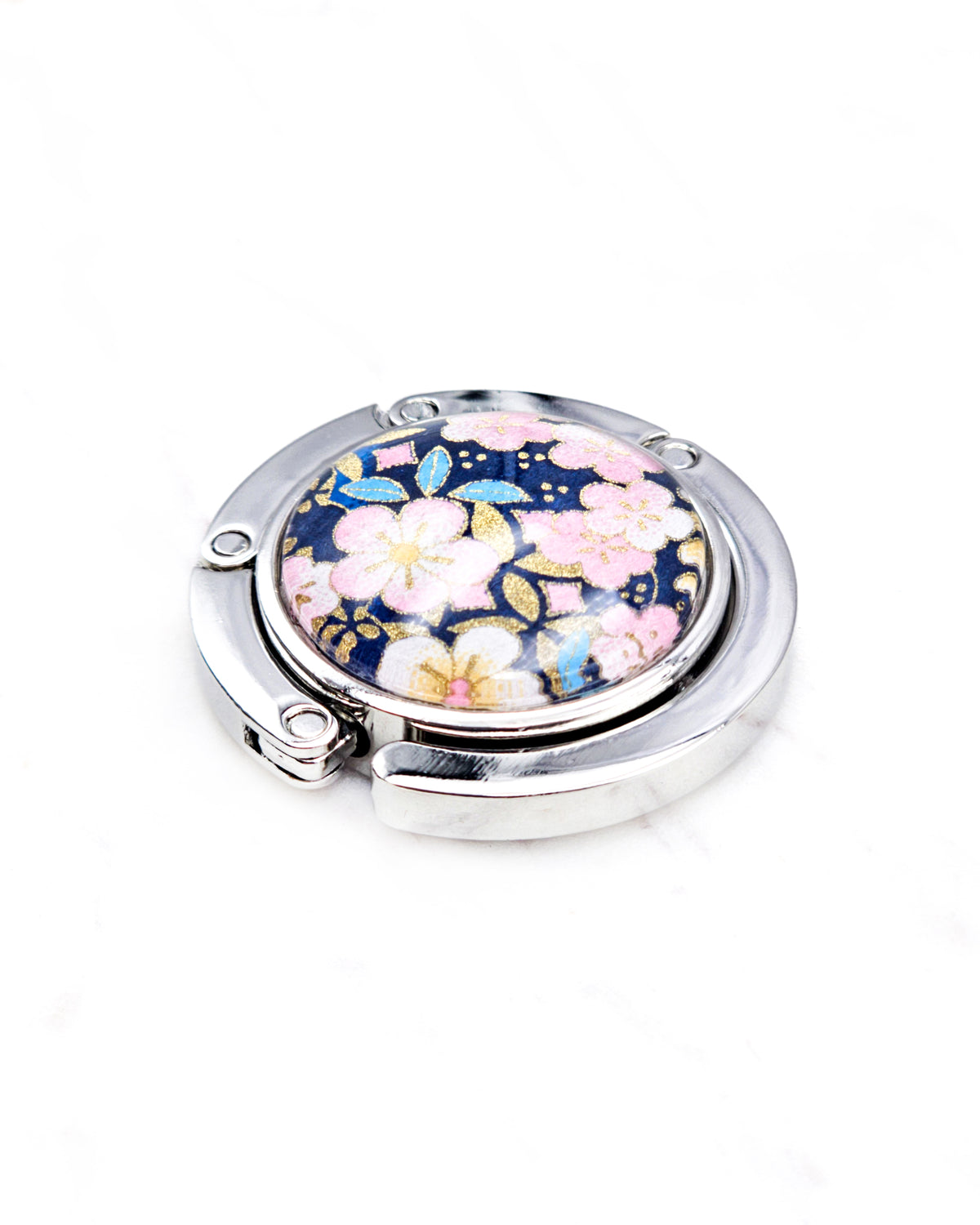 Round silver metal tabletop bag hanger featuring pink plum blossoms on a dark blue background with metallic gold details.