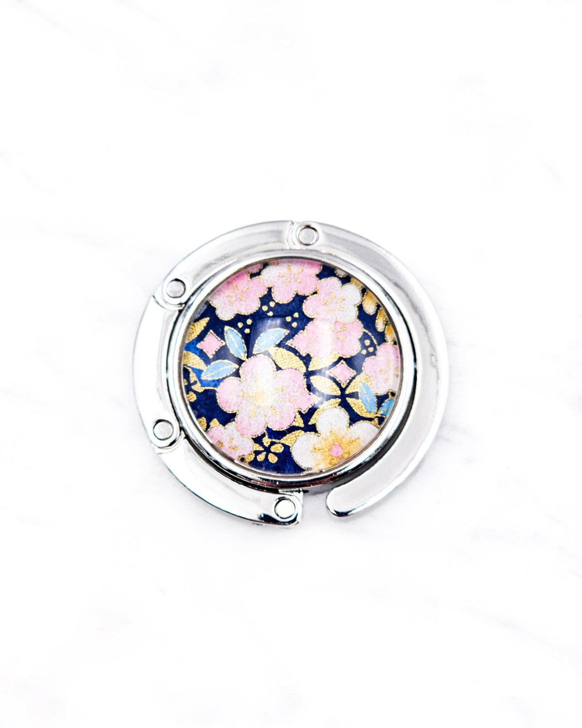 Round silver metal tabletop bag hanger featuring pink plum blossoms on a dark blue background with metallic gold details.