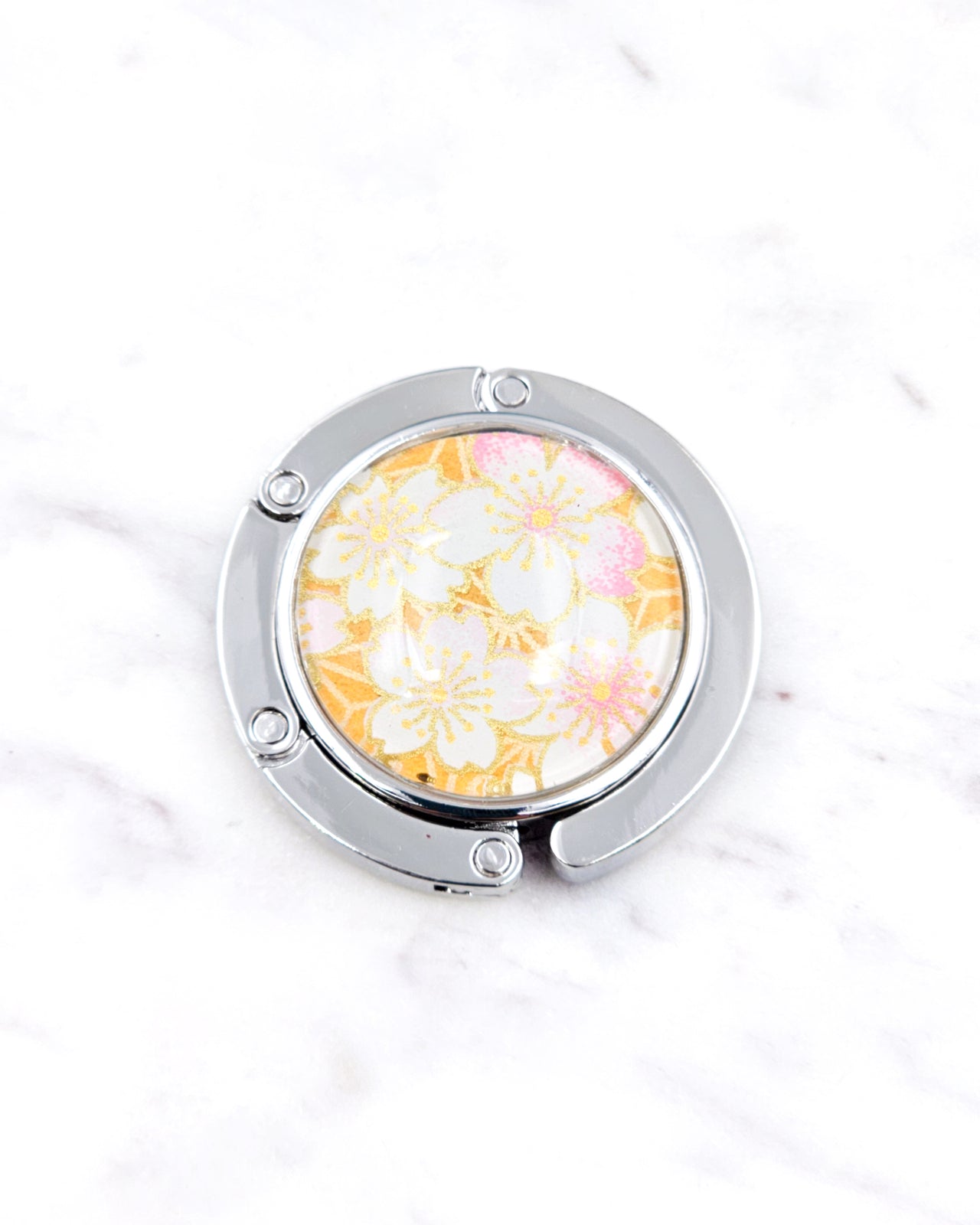 Silver metal table-top bag hanger featuring pink and white cherry blossoms on an orange background with metallic gold accents.
