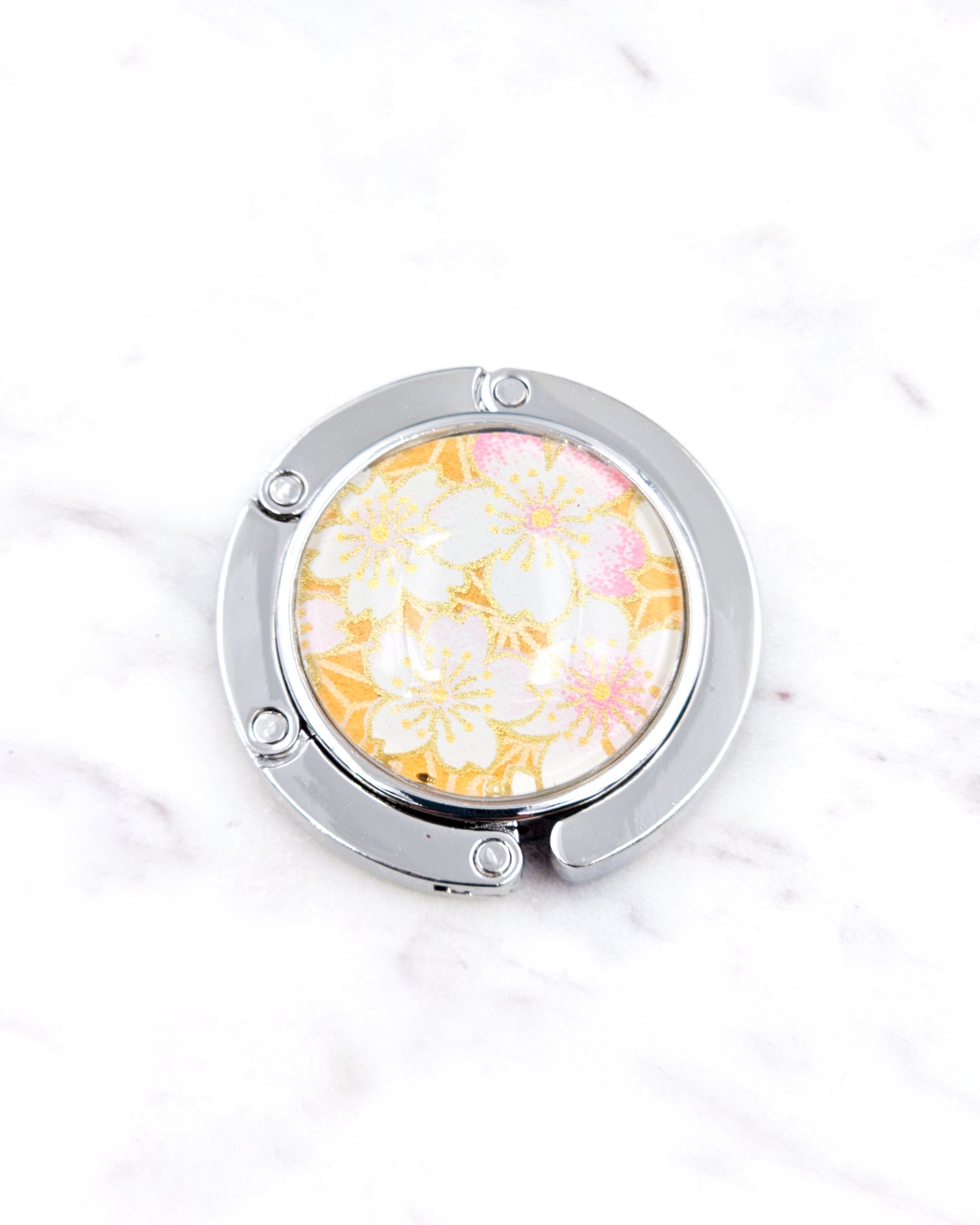 Silver metal table-top bag hanger featuring pink and white cherry blossoms on an orange background with metallic gold accents.