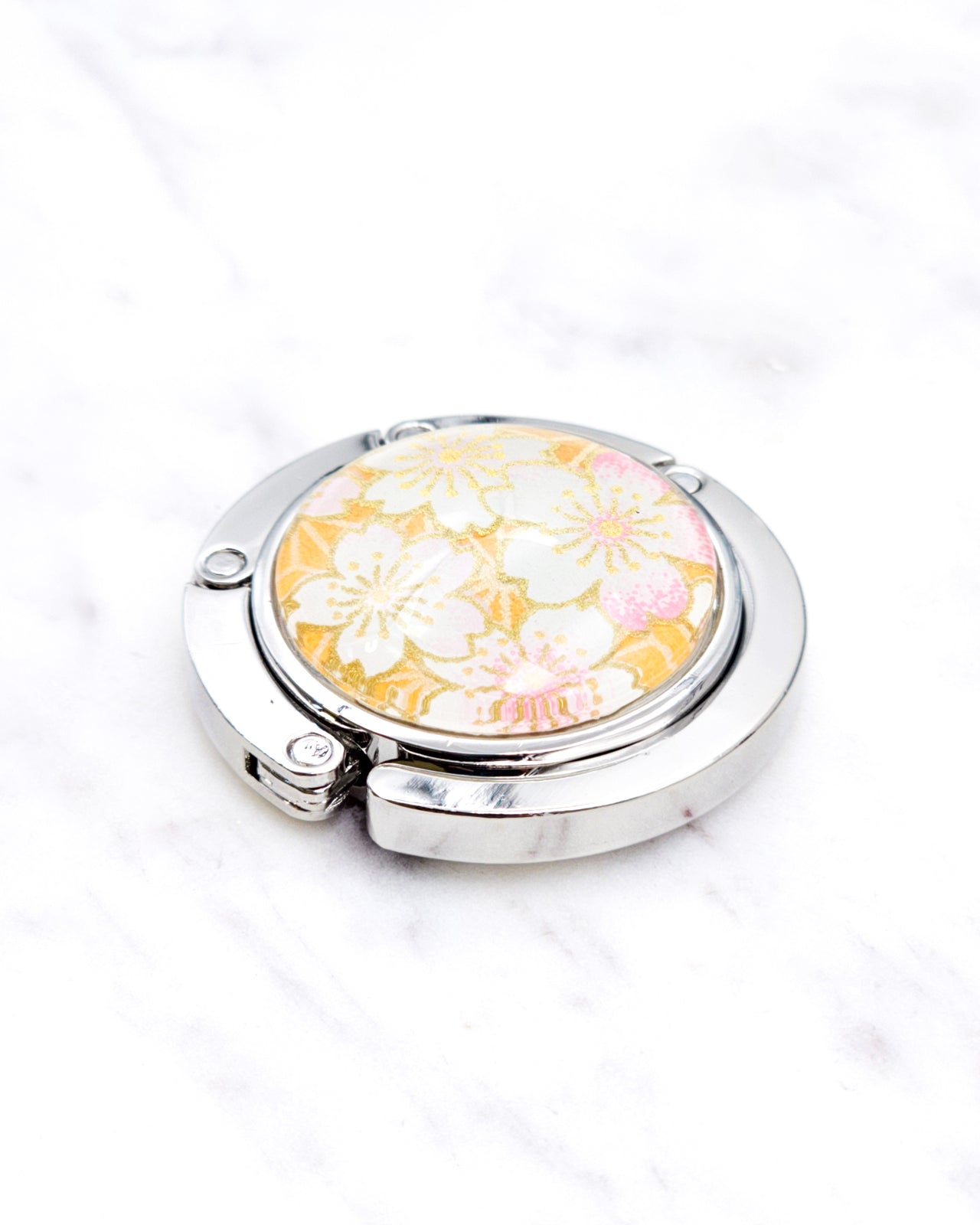Silver metal table-top bag hanger featuring pink and white cherry blossoms on an orange background with metallic gold accents.