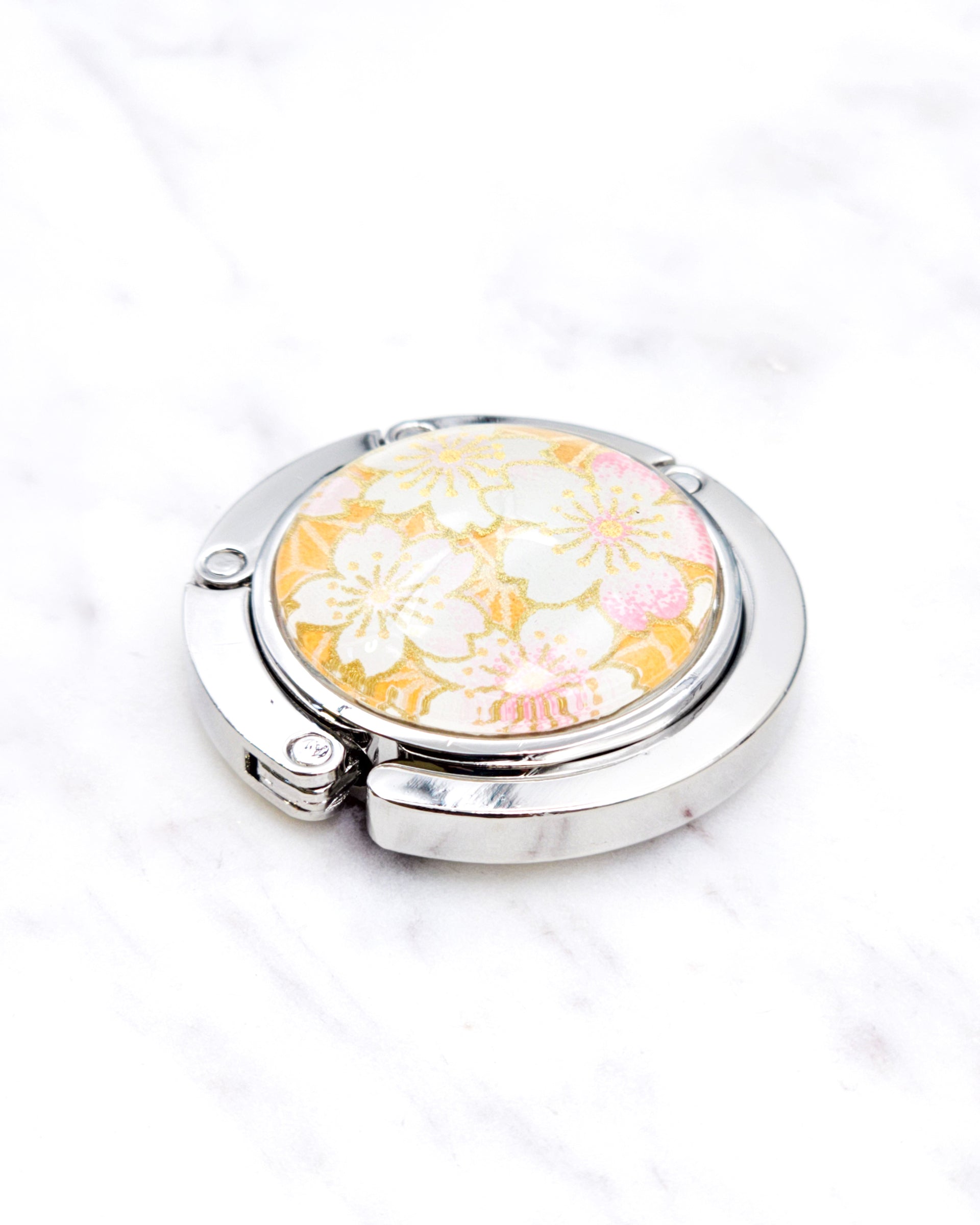 Silver metal table-top bag hanger featuring pink and white cherry blossoms on an orange background with metallic gold accents.