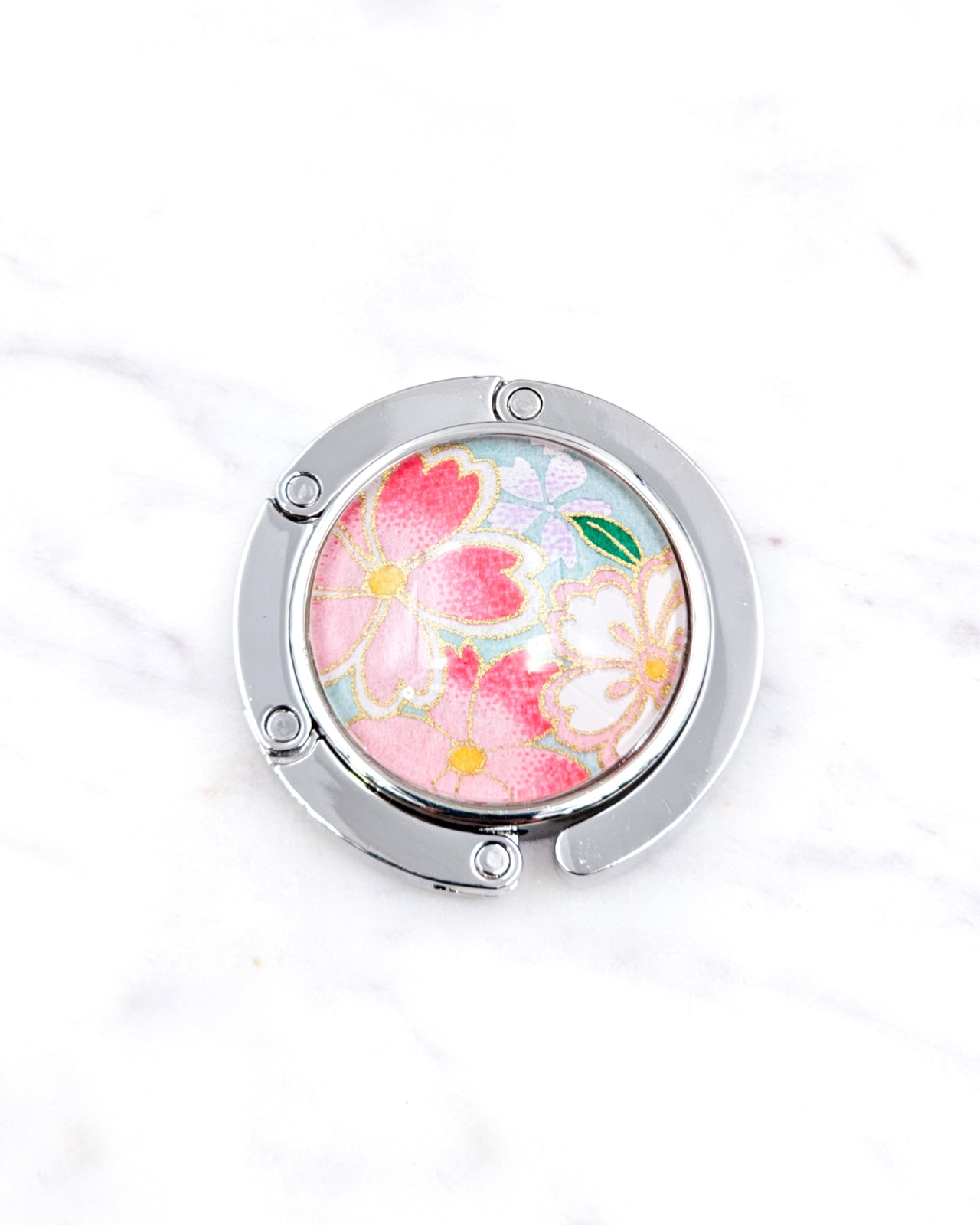 Silver metal table-top bag hanger featuring pink and white cherry blossoms on a turquoise blue background with metallic gold accents.