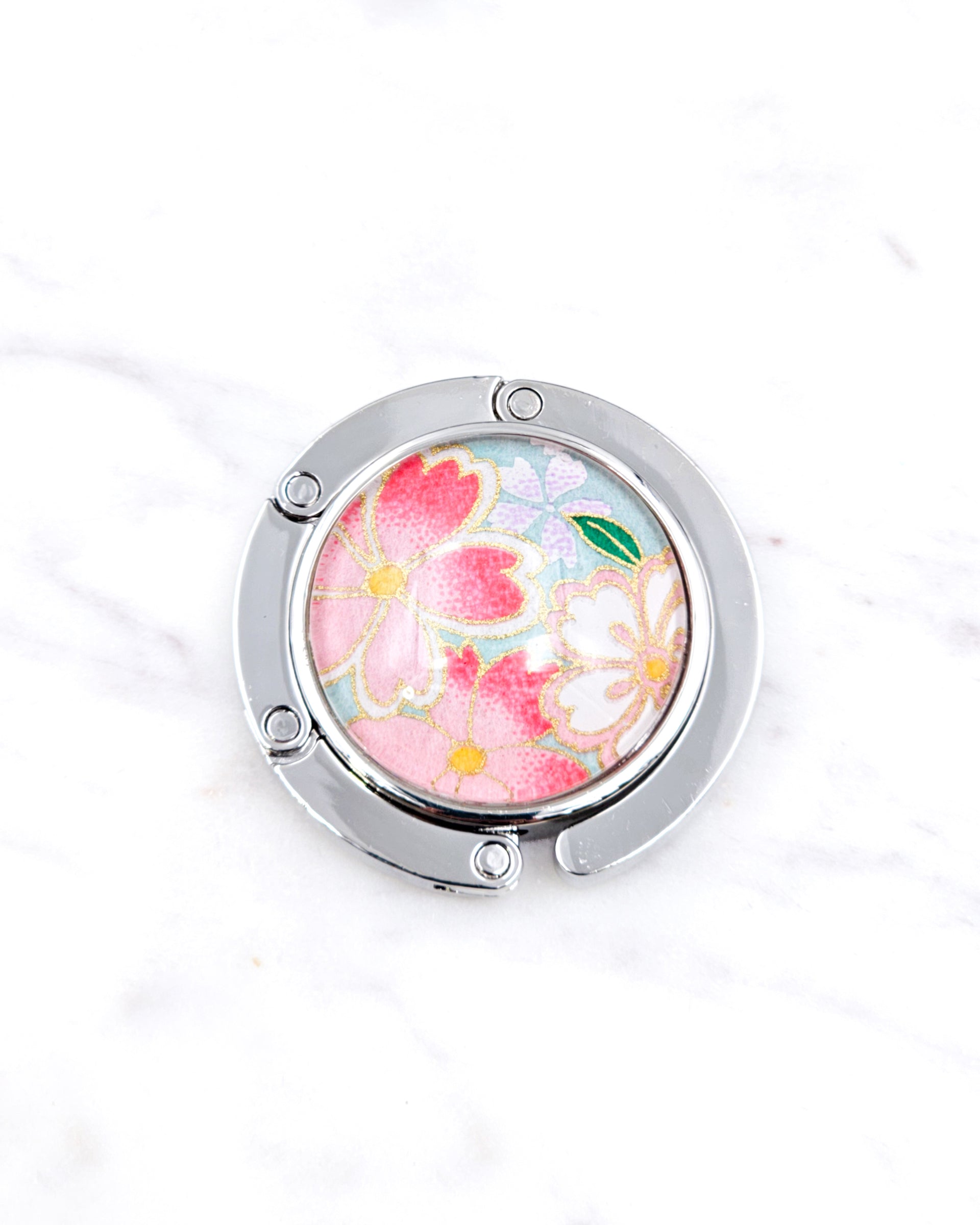 Silver metal table-top bag hanger featuring pink and white cherry blossoms on a turquoise blue background with metallic gold accents.