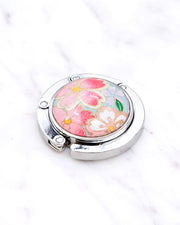 Silver metal table-top bag hanger featuring pink and white cherry blossoms on a turquoise blue background with metallic gold accents.