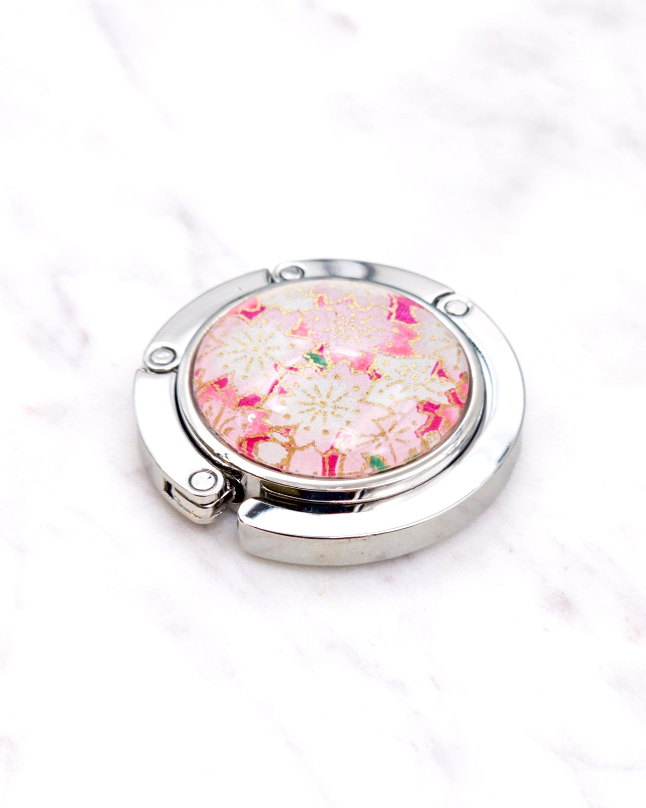 Silver metal table-top bag hanger featuring pink and white cherry blossoms on a pink background with metallic gold accents.