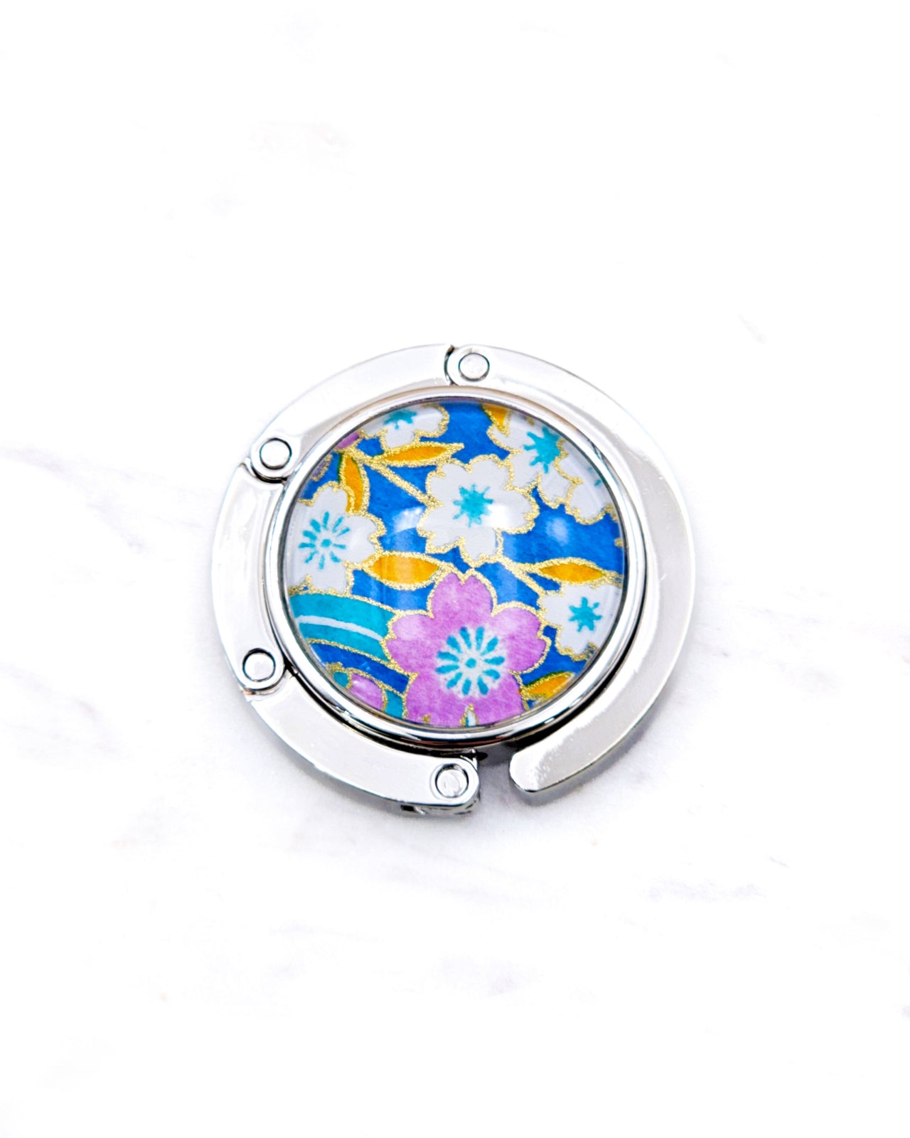 Round silver metal table-top bag hanger featuring pink and white cherry blossoms on a blue background with metallic gold details.