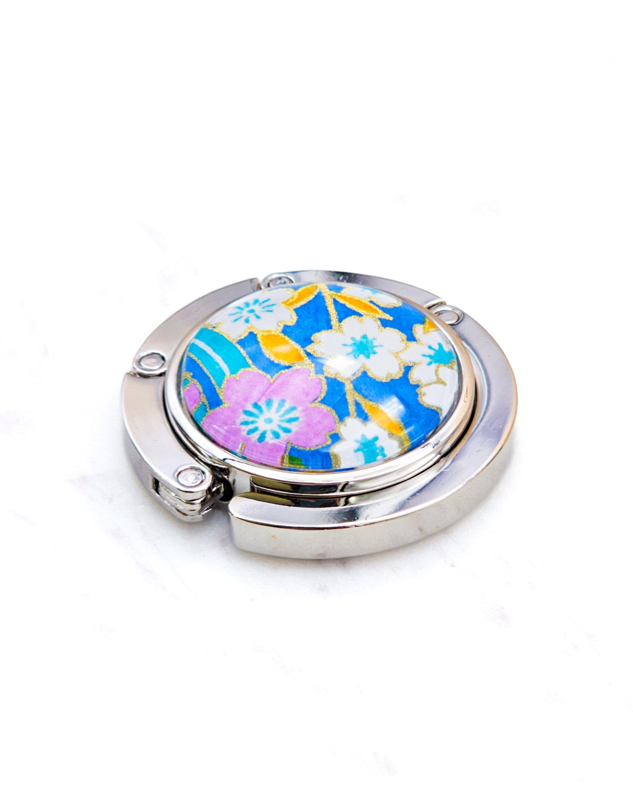 Round silver metal table-top bag hanger featuring pink and white cherry blossoms on a blue background with metallic gold details.