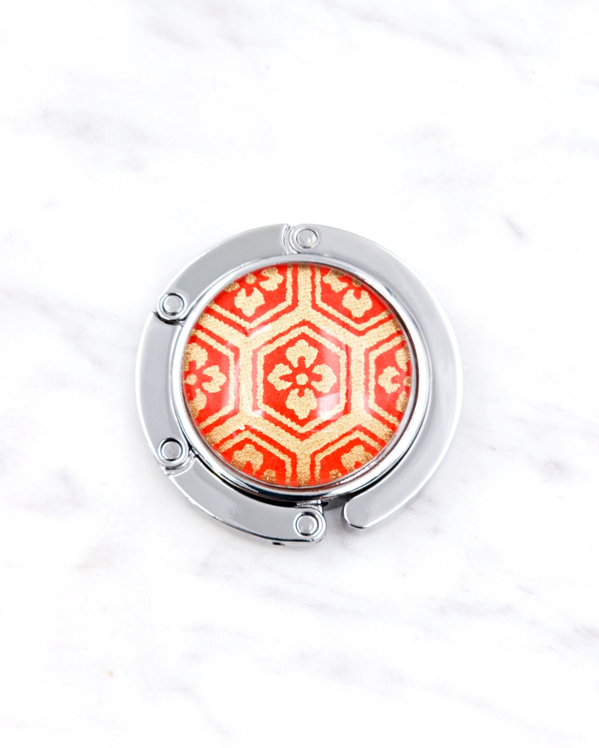 Silver metal table-top bag hanger featuring a traditional red and gold kikkou (tortoiseshell) design.