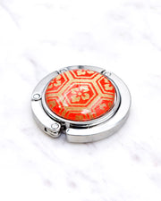 Silver metal table-top bag hanger featuring a traditional red and gold kikkou (tortoiseshell) design.