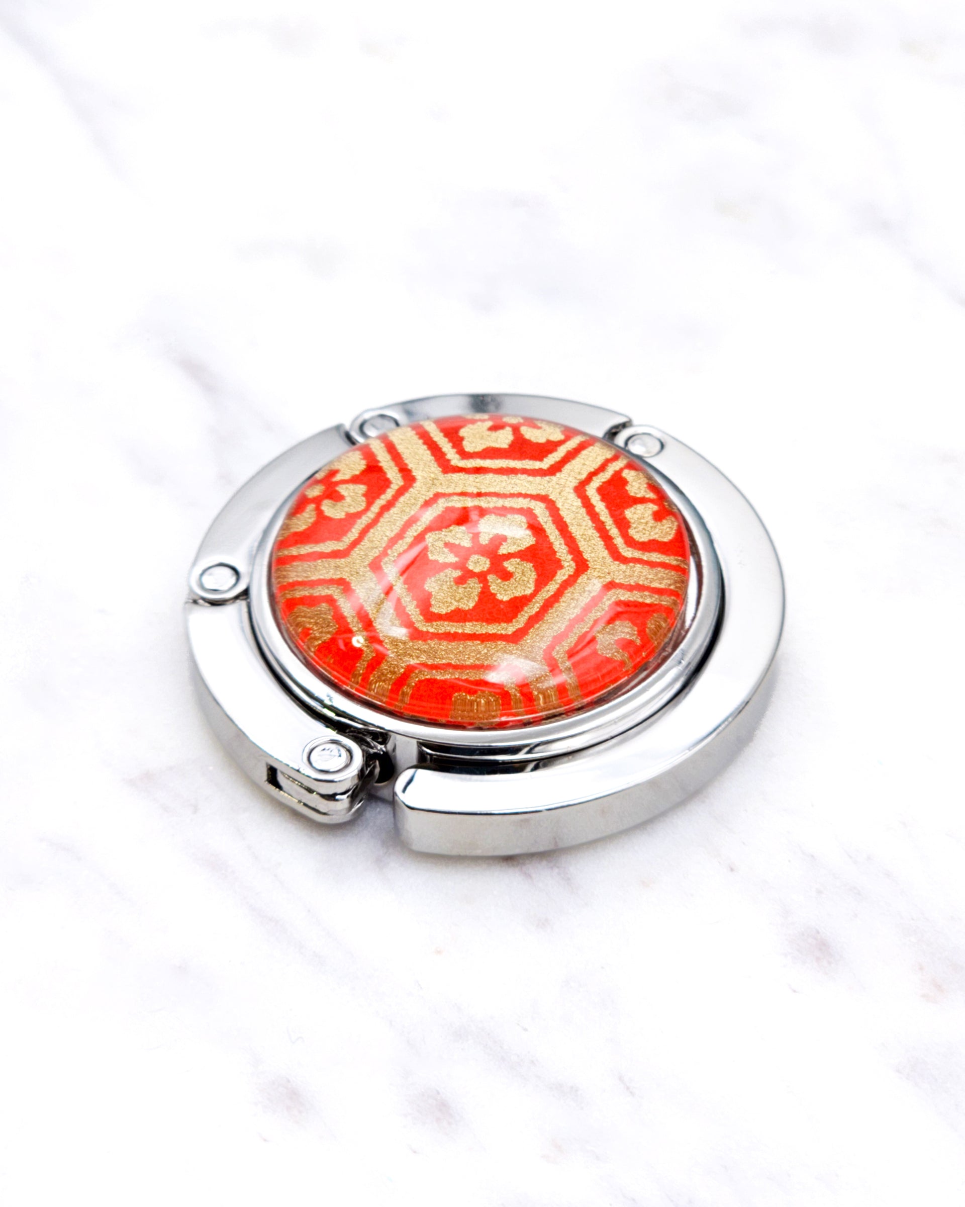 Silver metal table-top bag hanger featuring a traditional red and gold kikkou (tortoiseshell) design.