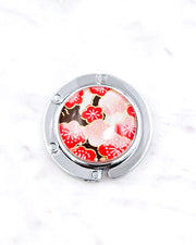 Silver metal table-top bag hanger featuring red plum blossoms on a white background with metallic gold accents.