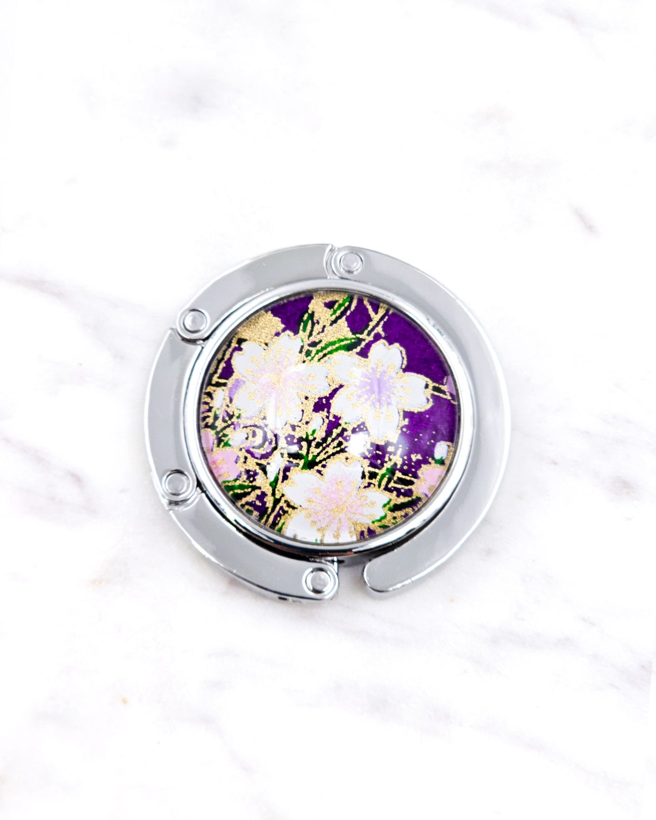 Silver metal table-top bag hanger featuring white cherry blossoms on a purple background with metallic gold accents.