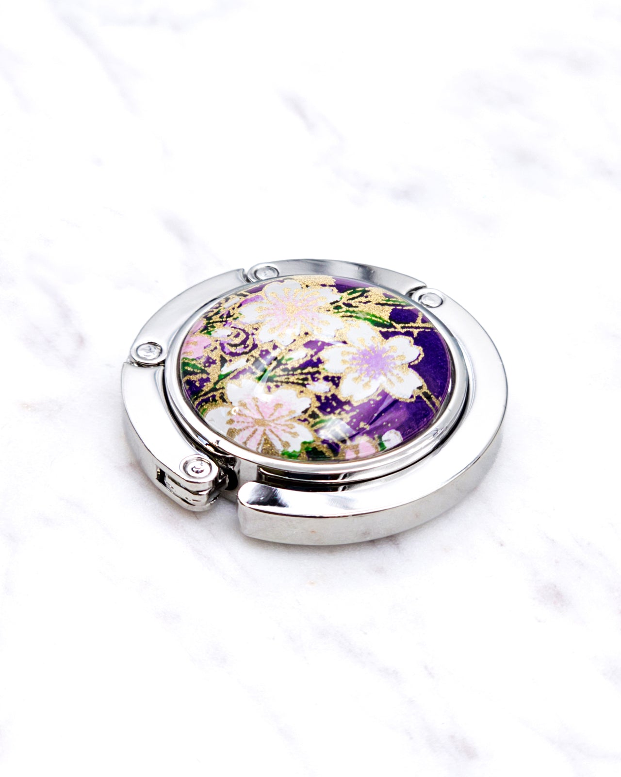 Silver metal table-top bag hanger featuring white cherry blossoms on a purple background with metallic gold accents.