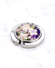 Silver metal table-top bag hanger featuring white cherry blossoms on a purple background with metallic gold accents.