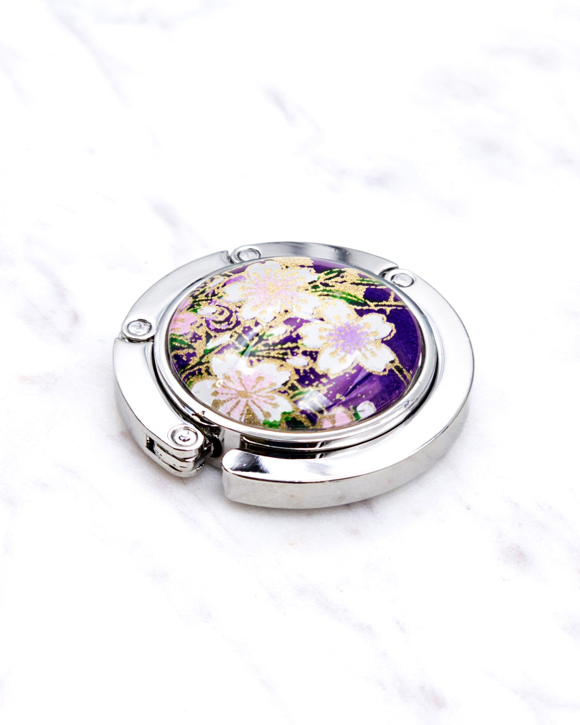 Silver metal table-top bag hanger featuring white cherry blossoms on a purple background with metallic gold accents.