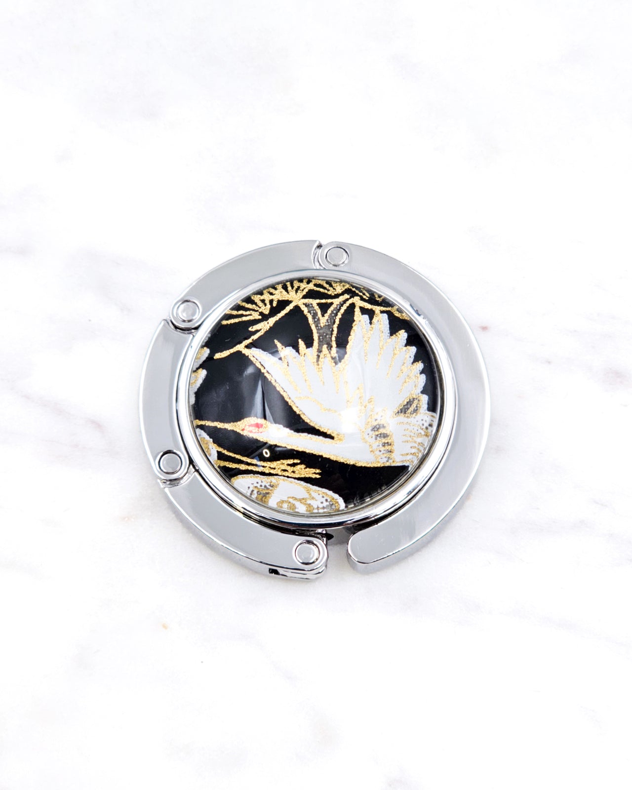 Silver metal table-top bag hanger featuring a white crane on a black background design with metallic gold accents.