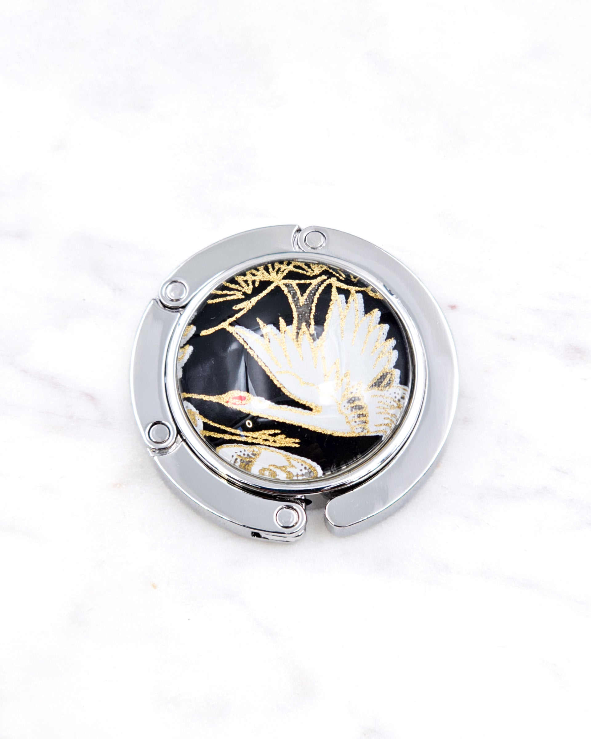 Silver metal table-top bag hanger featuring a white crane on a black background design with metallic gold accents.