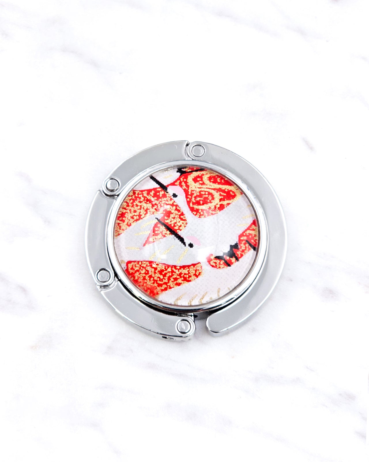 Silver metal table-top bag hanger featuring white flying cranes on a red background with metallic gold accents.