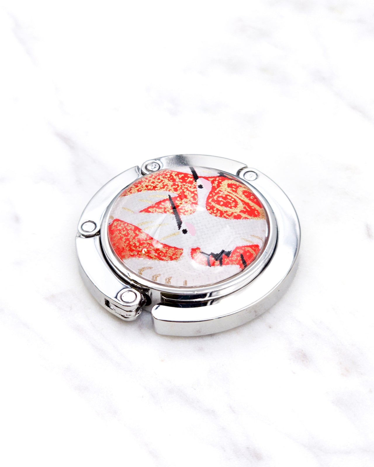 Silver metal table-top bag hanger featuring white flying cranes on a red background with metallic gold accents.