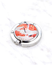 Silver metal table-top bag hanger featuring white flying cranes on a red background with metallic gold accents.