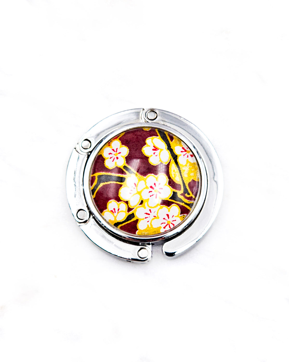Round silver metal tabletop bag hanger featuring white plum blossoms and black branches on a brown background with metallic gold details.