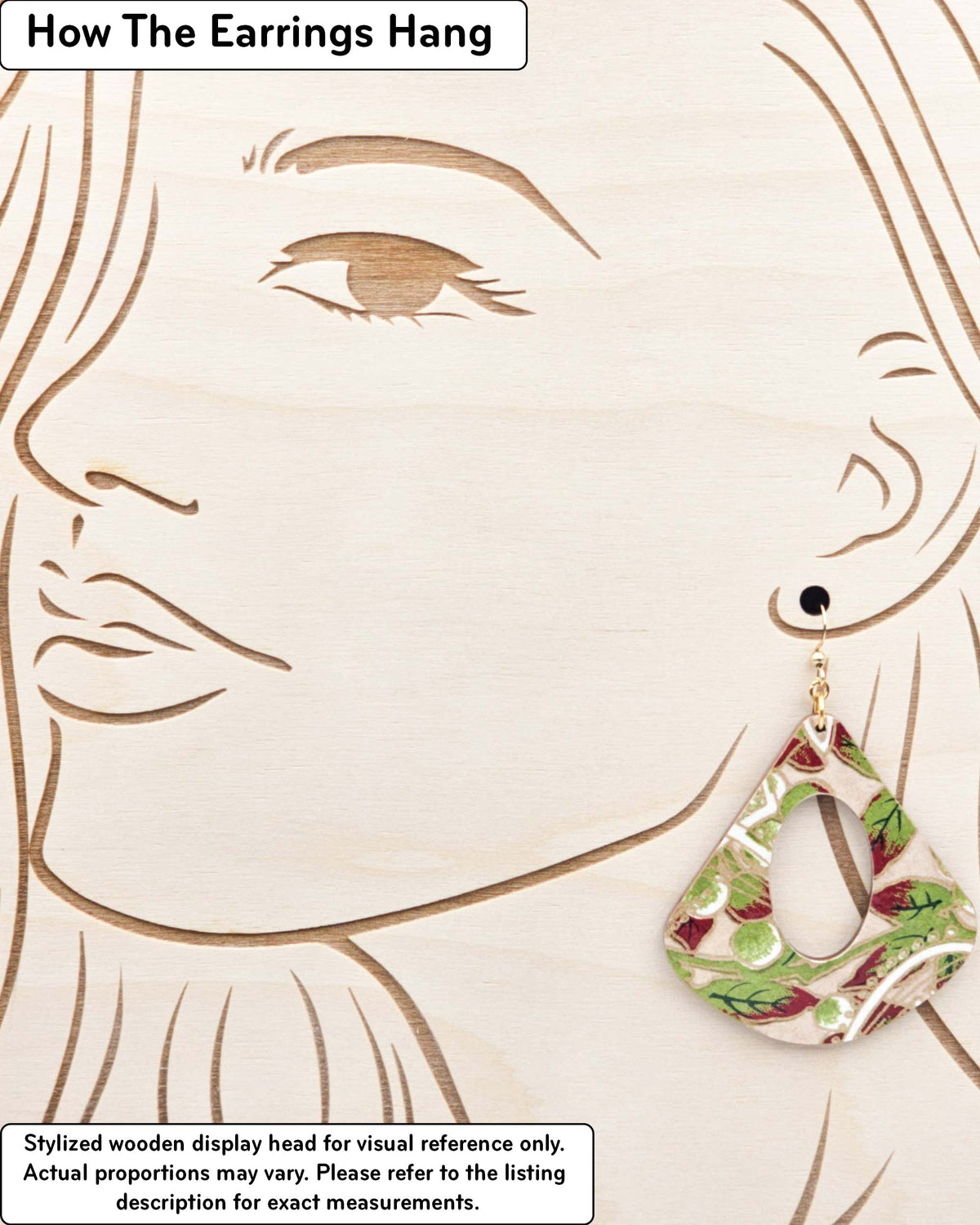 X-Large wooden hollow rounded triangle shaped earrings featuring green leaves with red tips and white swirls on a brown background with metallic gold details, displayed on a stylized wooden head to demonstrate how the earring hangs when worn. Display is not to scale.