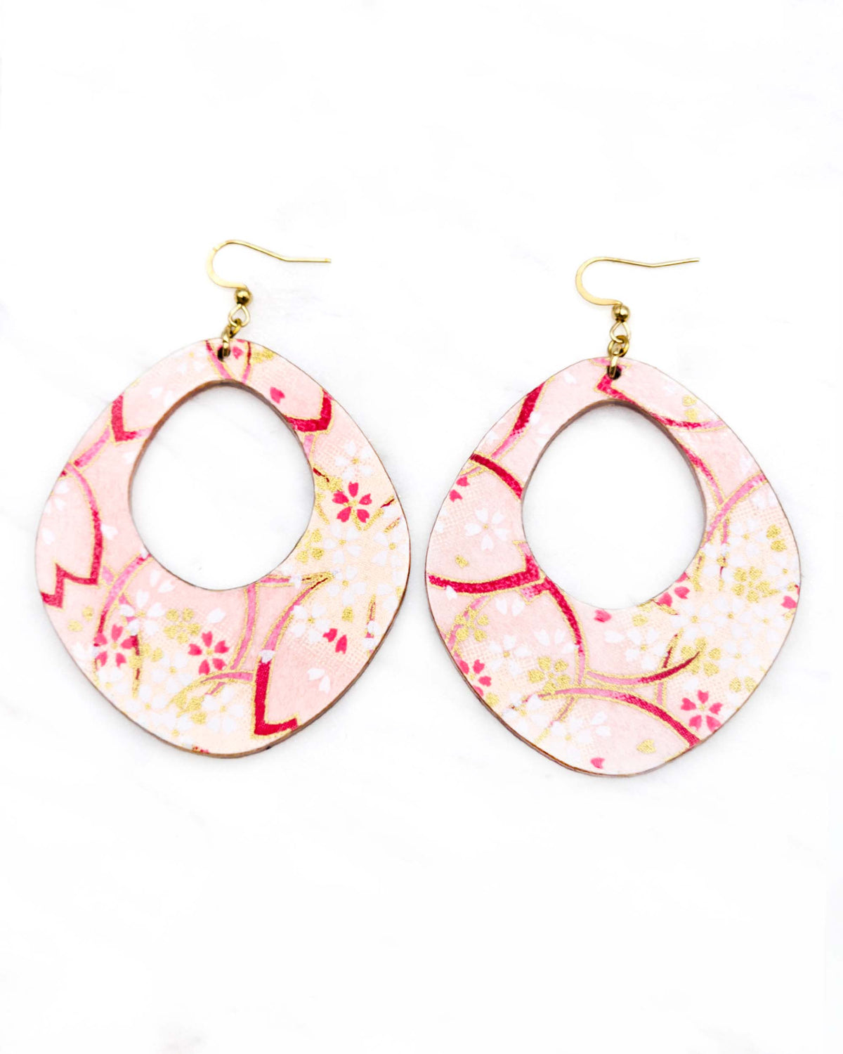X-Large wooden abstract hoop shaped earrings featuring small white and gold cherry blossoms and large pink cherry blossom outlines on a light pink background with metallic gold details.