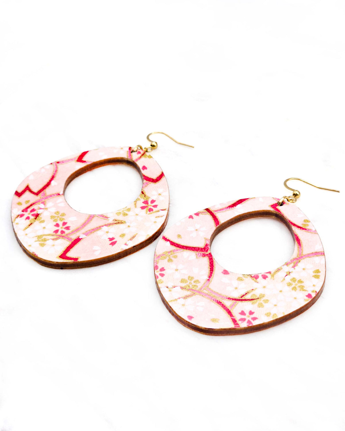X-Large wooden abstract hoop shaped earrings featuring small white and gold cherry blossoms and large pink cherry blossom outlines on a light pink background with metallic gold details.