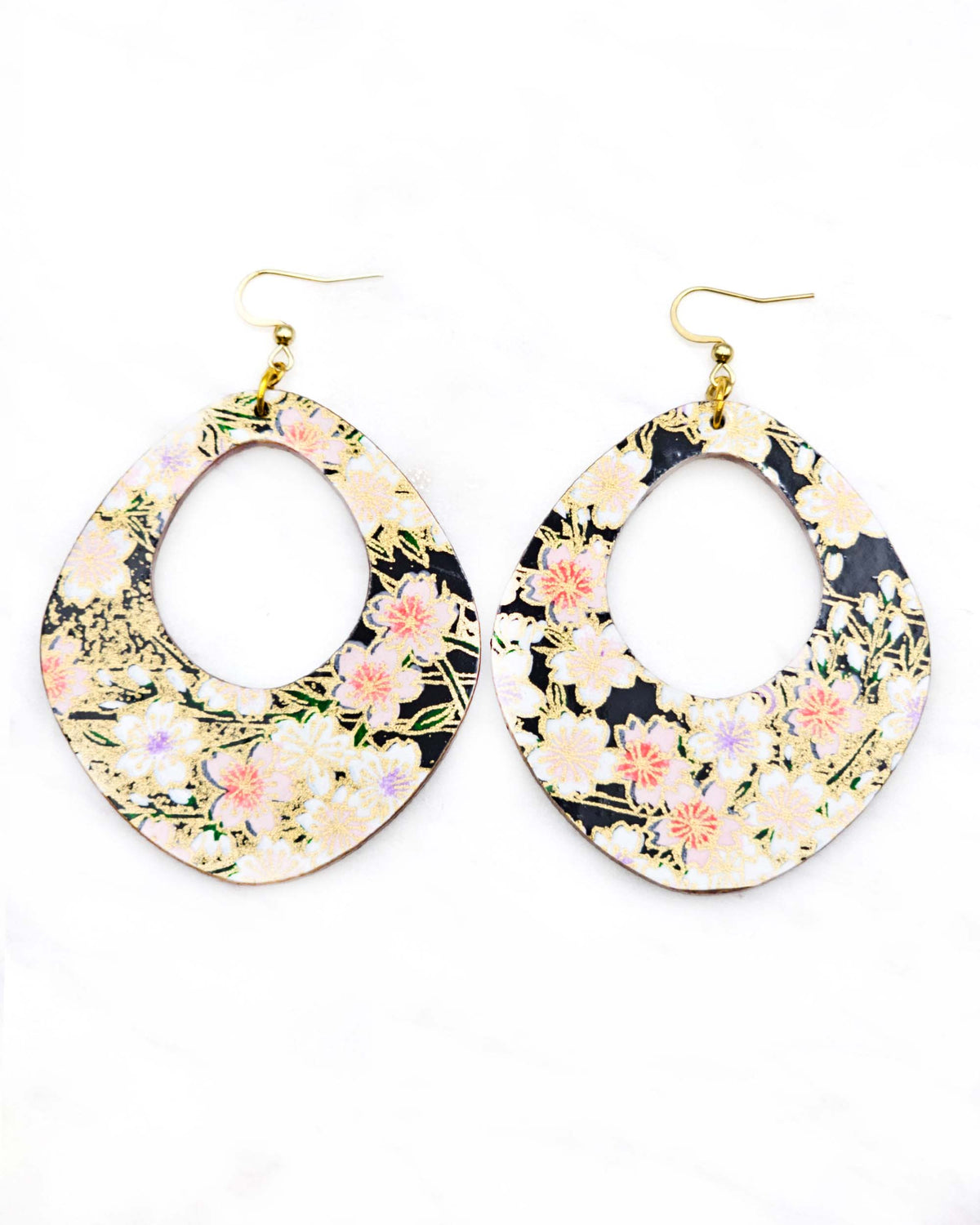 X-Large wooden abstract hoop shaped earrings featuring pink cherry blossoms and white cherry blossoms with purple and pink centers on a black background with metallic gold details.