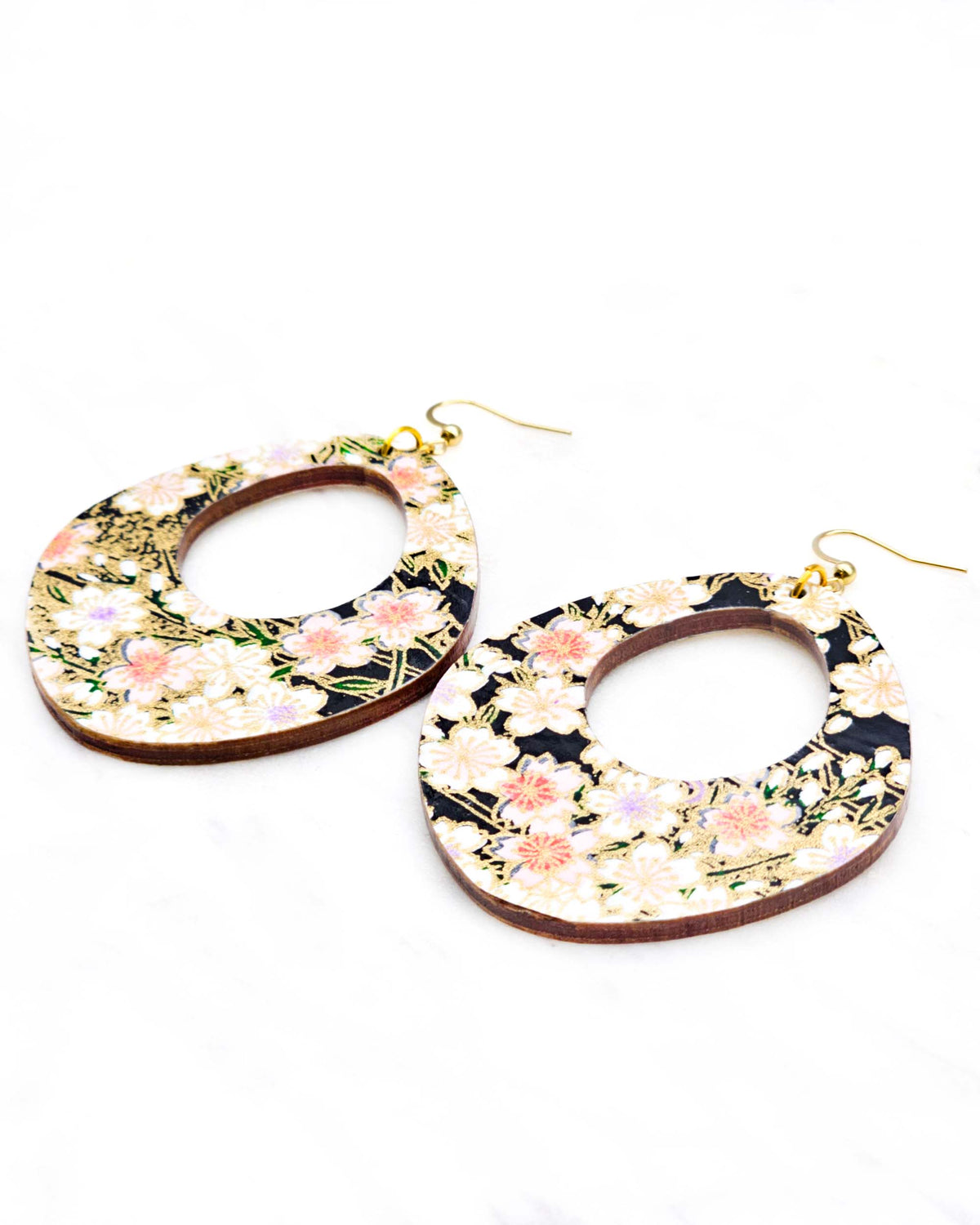 X-Large wooden abstract hoop shaped earrings featuring pink cherry blossoms and white cherry blossoms with purple and pink centers on a black background with metallic gold details.